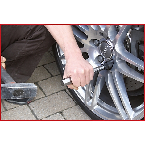 Eine Person schraubt an einem silbernen Autorad. Ein Hammer liegt daneben.